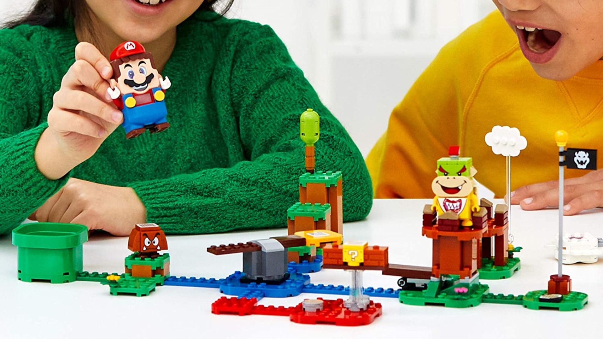 A couple of children joyfully playing with a LEGO Mario set.