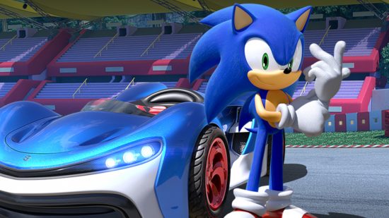 Najlepsze gry Sonic: Zrzut ekranu ze strony internetowej Team Sonic Racing przedstawiający Sonica stojącego obok niebieskiego samochodu wyścigowego na arenie.
