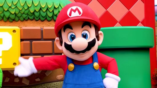 Nintendo Universal relationship header showing a man in a mario costume -- red hat and shirt, white gloves, blue dungarees, big black moustache, round nose and cartoon eyes, in front of a block made of bricks, a block with a question mark on it, a green pipe into the ground, all in front of a red wall, as Mario waves his left hand and keeps his right on his hip.