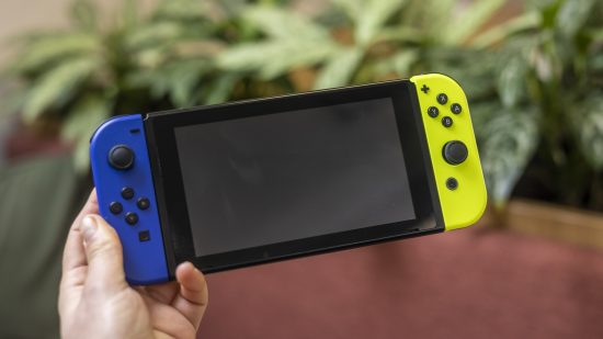 Nintendo Switch console being held in front of a blurry background