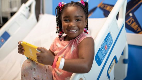 A little girl in a hospital bed playing a yellow Nintendo Switch.
