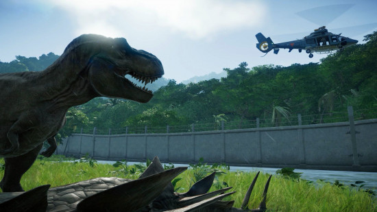Giochi di Jurassic World: un T-rex osserva un elicottero sopra una recinzione alla fine di un prato, di fronte a una fitta giungla.