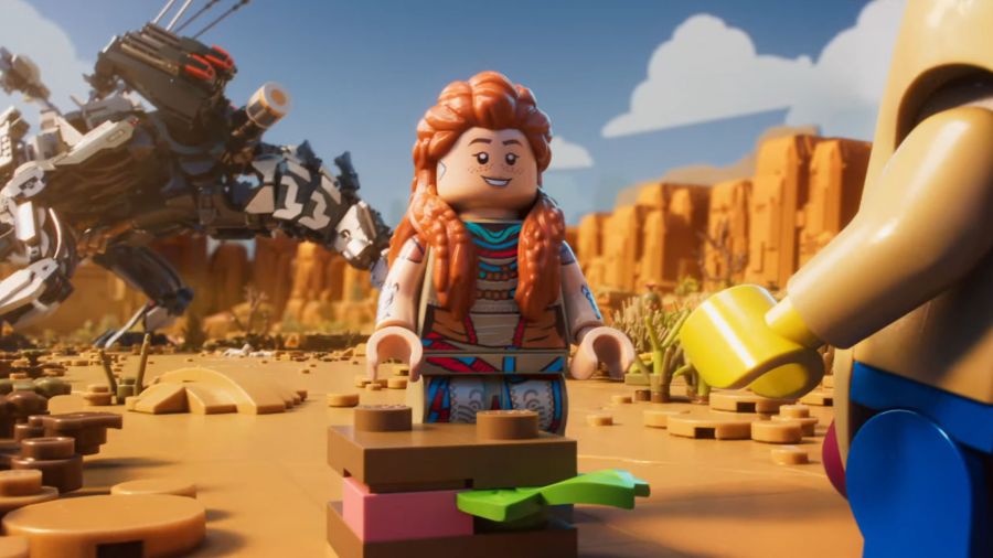A screenshot of Lego Horizon Adventures showing Aloy standing in front of a huge monster and smiling