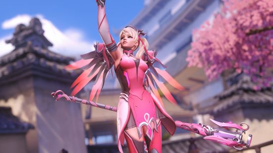 Overwatch 2 Pink Mercy: A screenshot of OG Pink Mercy doing her resurrect pose in front of Hanamura's second capture point with a cherry blossom tree off to the right. She is in focus and the background is blurred