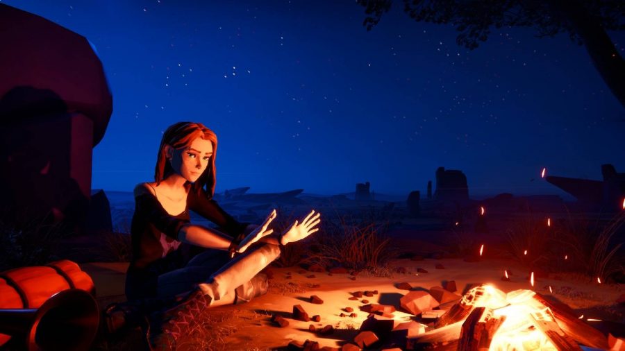 A young female with red hair is sat in front of a campfire, holding up their hands to warm them 